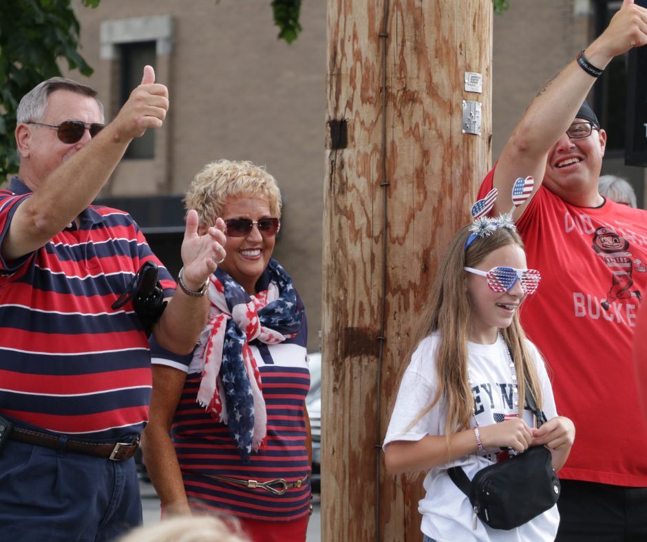 A family of four in red, white, and blue cheering while watching a parade