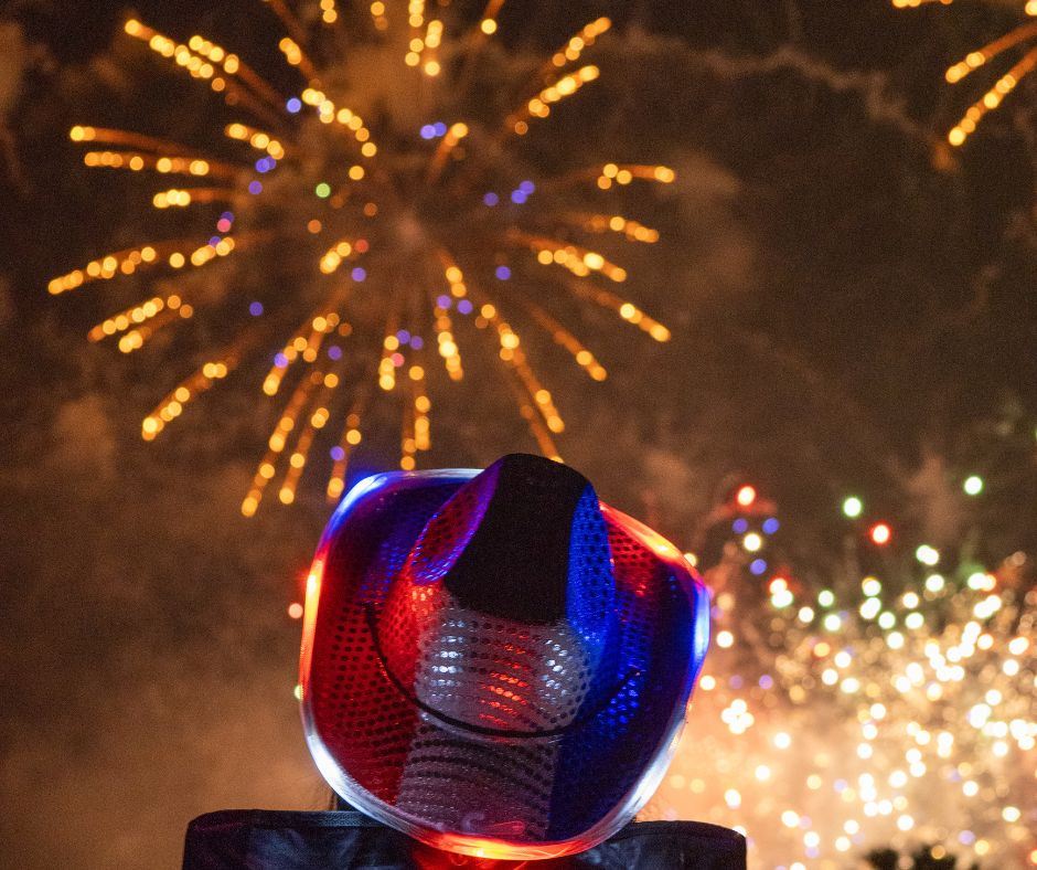 A person in a red, white, and blue cowboy hat watching fireworks in the night sky