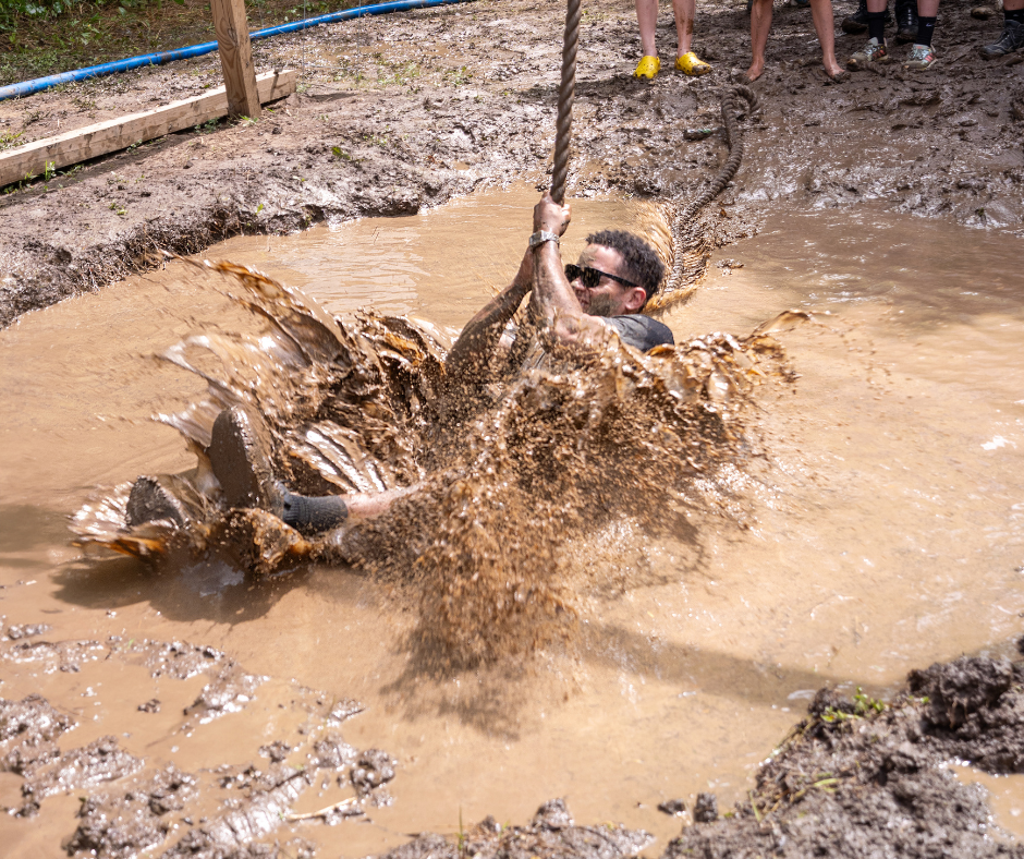 A man splashing into a mud puddle trying to swing over it