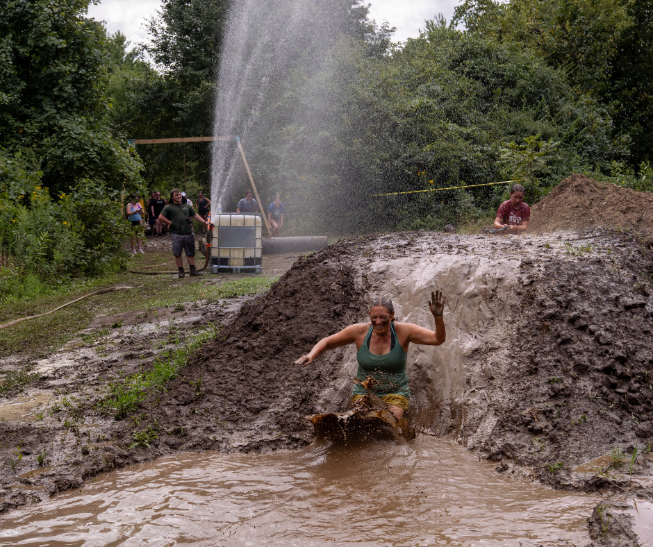 Woman sliding down a hill of mud into a large puddle of mud