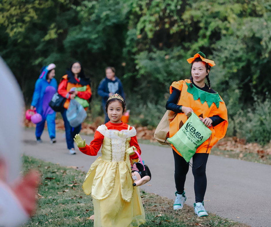 Photo of families walking on the trick or treat trail and a little girl waving
